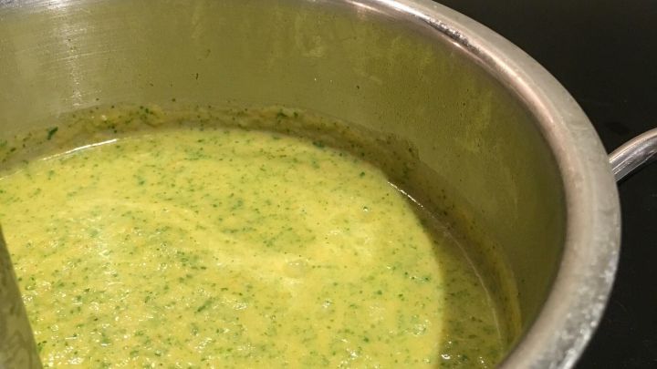 Eine gr&uuml;ne Gem&uuml;secremesuppe wird mit einem P&uuml;rierstab in einem Topf auf dem Herd p&uuml;riert, um eine leichte, gesunde Mahlzeit zu kreieren.