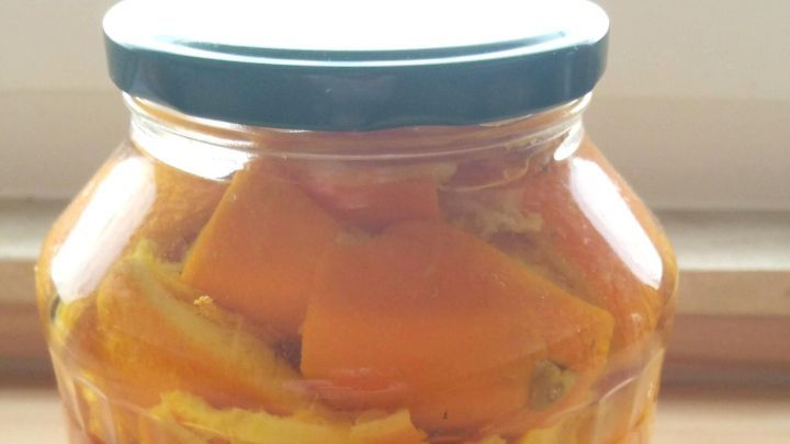 Ein Glas mit orangenen Orangenschalen befindet sich auf einem Holztisch und wird zur Herstellung von Entkalker und Reiniger genutzt.