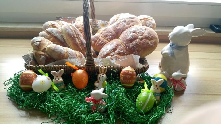 Frische Schmand-Br&ouml;tchen liegen in einem Korb, umgeben von bunte Ostereiern und einem kleinen Hasen auf gr&uuml;nem Gras.