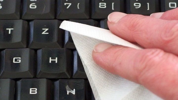 Eine Hand h&auml;lt ein feuchtes Allzwecktuch, das gerade &uuml;ber die Tasten einer PC-Tastatur wischt und sie reinigt.