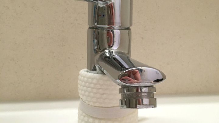 Ein gl&auml;nzender Wasserhahn tropft und steht auf einem Waschbeckenrand, umgeben von einer schlichten Wand.