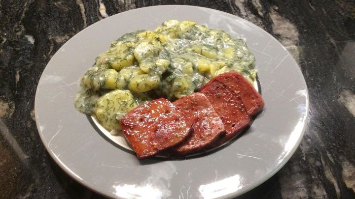 Auf einem grauen Teller liegen Dillkartoffeln, umgeben von einer cremigen So&szlig;e, und einige Scheiben Fleisch.