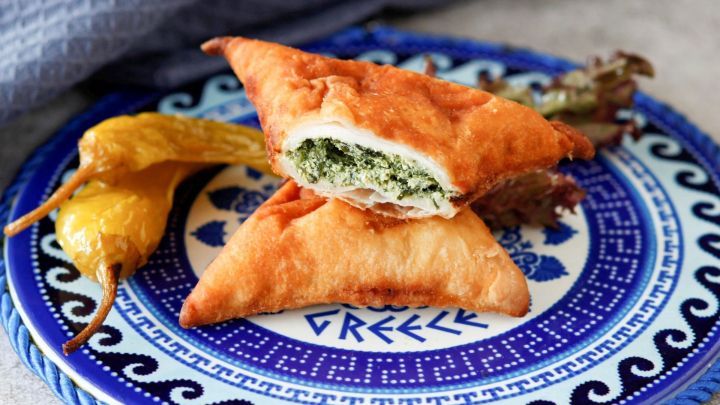 K&auml;seteigtaschen liegen auf einem bunten Teller, w&auml;hrend eine aufgeschnittene Tasche den cremigen Inhalt zeigt.