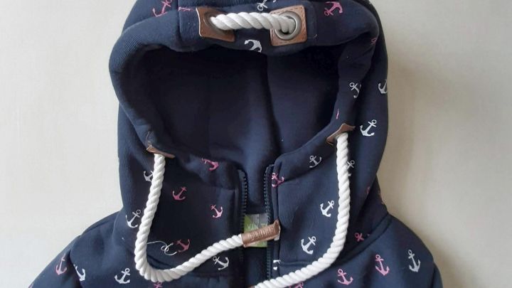 Die Sweatshirtjacke mit Kapuze hat eine Kordel, die herausgezogen werden sollte, auf navyblauem Stoff mit Anker-Muster.