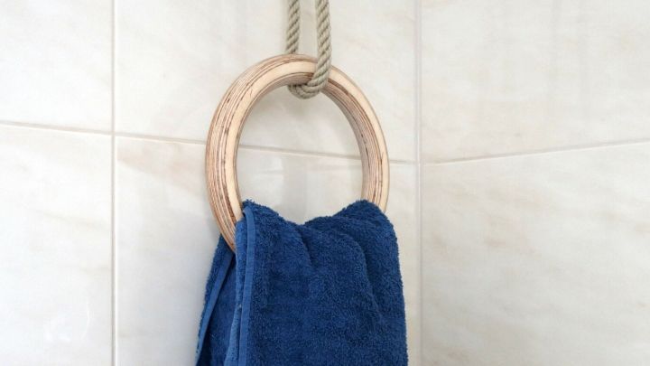Ein Holzring h&auml;ngt an einem Seil an der Wand, w&auml;hrend ein blaues Handtuch daran h&auml;ngt und das Badezimmer dekoriert.