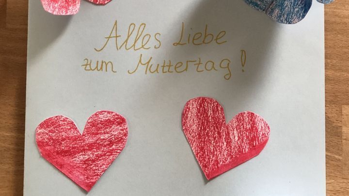 Auf einer Karte sind liebevoll gezeichnete Herzen und Papierblumen arrangiert, um "Alles Liebe zum Muttertag!" zu sagen.