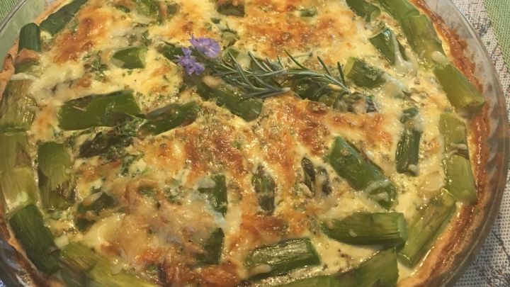 Eine Tarte mit gr&uuml;nem Spargel liegt auf einem dekorativen Tischl&auml;ufer, umgeben von einem Getr&auml;nk im Hintergrund.