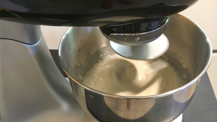 Ein K&uuml;chenmaschinen-Metallbeh&auml;lter mit Teig, der gemischt wird, w&auml;hrend sich der Mixer auf einer Arbeitsfl&auml;che befindet.