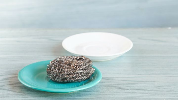 Eine Stahlwolle liegt auf einem t&uuml;rkisfarbenen Teller, w&auml;hrend ein leerer wei&szlig;er Teller daneben auf einem hellen Tisch steht.