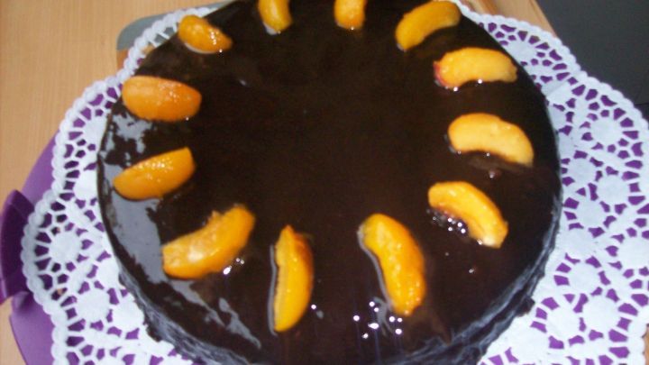 Die Schokotorte nach Sacher Art liegt auf einer dekorativen Serviette und ist mit glattem Schokoladenguss und Aprikosenspalten verziert.