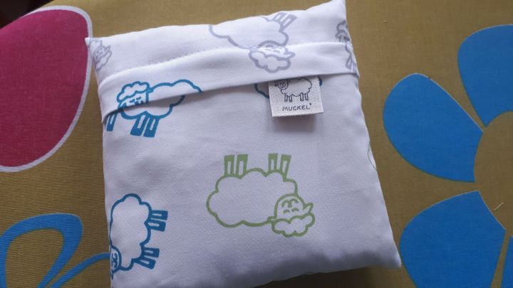 Ein W&auml;rmekissen mit Schafswolle liegt auf einem bunten Untergrund, dekoriert mit niedlichen Schaf-Motiven.