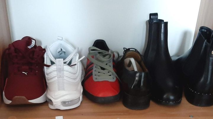Rote Sneakers, wei&szlig;e Sportschuhe und schwarze Stiefel stehen ordentlich nebeneinander auf einem Holzregal zur platzsparenden Aufbewahrung.