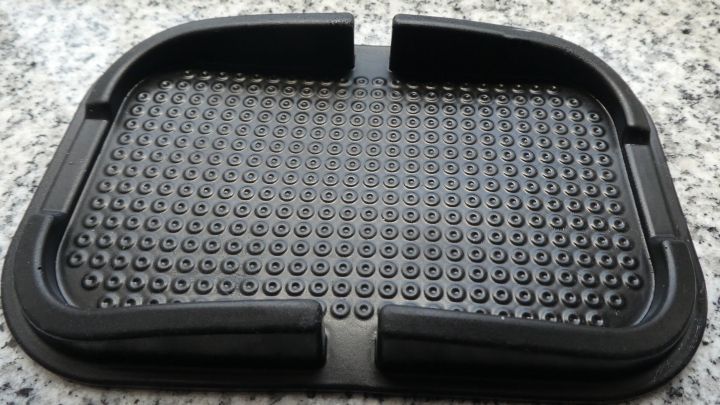 Eine schwarze, selbsthaftende Antirutschmatte liegt auf einer glatten, hellen Oberfl&auml;che und zeigt eine strukturierte Oberfl&auml;che.