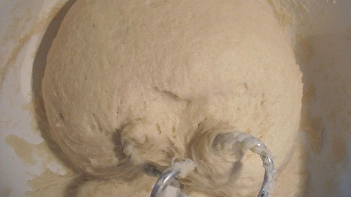 Ein gro&szlig;er Hefeteig ruht in einer Sch&uuml;ssel, w&auml;hrend R&uuml;hrhaken ihn sanft durchkneten. Die Textur ist weich und geschmeidig.