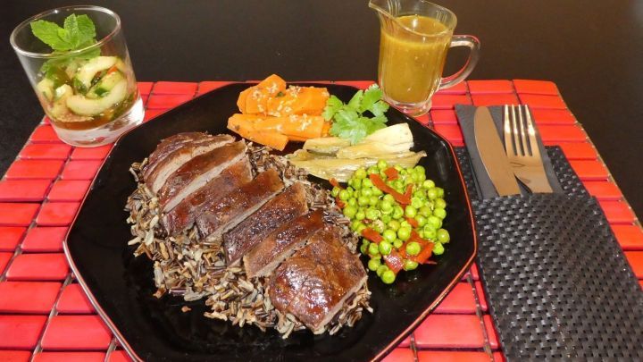 Auf einem schwarzen Teller liegen saftig in Scheiben geschnittene G&auml;nsebrust, umgeben von buntem Gem&uuml;se und Reis.