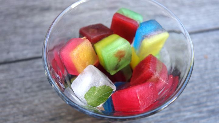 Bunte Eisw&uuml;rfel liegen in einer Sch&uuml;ssel und funkeln in verschiedenen Farben, perfekt f&uuml;r erfrischende Getr&auml;nke.