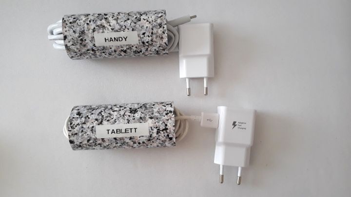 Zwei Ladekabel sind ordentlich verstaut in h&uuml;bschen H&uuml;llen, verbunden mit wei&szlig;en Netzteilen auf einem hellen Untergrund.