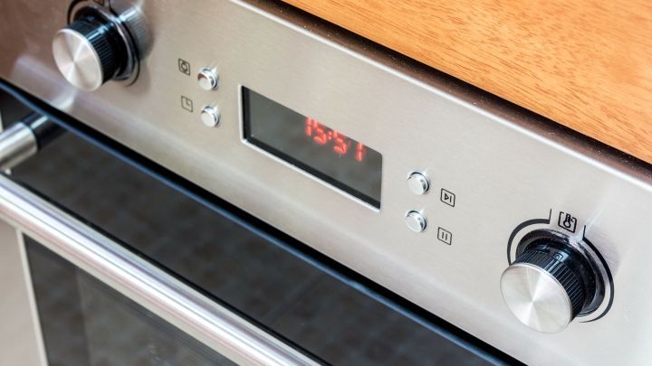 Edelstahl-Ofen mit Bedienelementen, der gerade auf eine Temperatur eingestellt wird, auf einer Holzoberfl&auml;che.