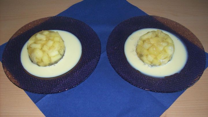 Zwei Schalen mit Apfelw&uuml;rfeln in Apfelsaft-Gelee liegen auf einem blauen Tischtuch, umgeben von dekorativen Tellern.