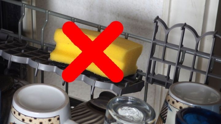 Ein gelber Schwamm liegt in einer Sp&uuml;lmaschine, umgeben von Gl&auml;sern und Tassen, mit einem roten Kreuz markiert.