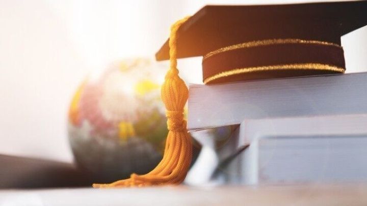 Ein Doktorhut liegt auf gestapelten B&uuml;chern, w&auml;hrend im Hintergrund eine Weltkugel zu sehen ist, symbolisch f&uuml;r das Studium.