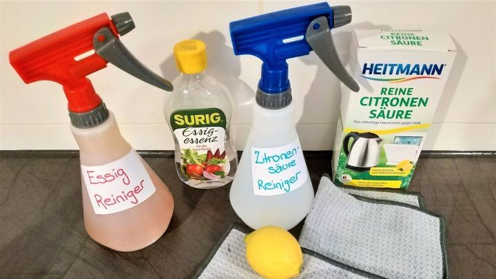 Spr&uuml;hflaschen mit selbstgemachten Putzmitteln stehen neben Zitronen und Mikrofasert&uuml;chern auf einer Holzoberfl&auml;che, bereit zum Reinigen.