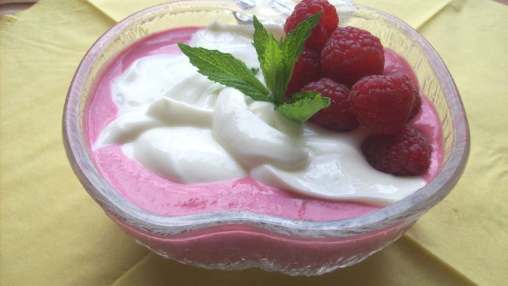 Ein pinkes Quark-Frischk&auml;se-Dessert in einer Schale, garniert mit Himbeeren und Minze, auf einem gelben Untergrund.