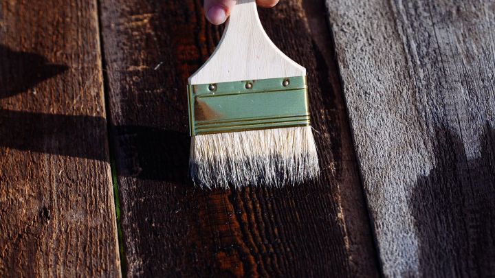 Ein Pinsel streicht Holzschutzlasur auf eine Holzoberfl&auml;che im Freien, um die Oberfl&auml;che zu sch&uuml;tzen und zu verbessern.