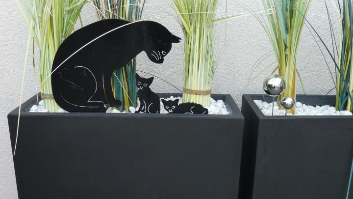Schwarzer Pflanzencontainer aus Fiberglas mit Gras und Katzenmotiv im Vordergrund, im modernen Au&szlig;enbereich platziert.