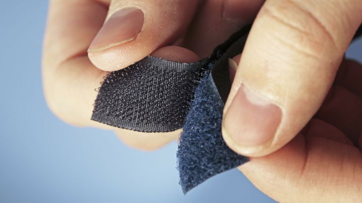 Eine Hand h&auml;lt zwei Teile von Klettverschluss, die gerade getrennt werden, auf einem blauen Hintergrund.