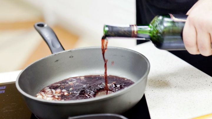 Rotwein wird in eine Pfanne gegossen, um in der K&uuml;che So&szlig;en f&uuml;r besseren Geschmack zuzubereiten.