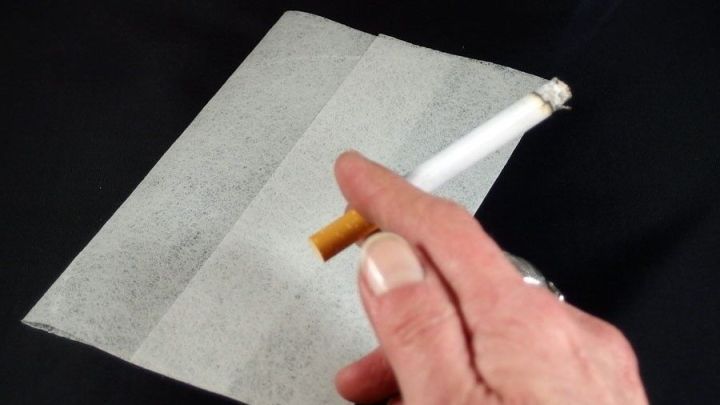 Eine Hand h&auml;lt eine Zigarette &uuml;ber einem Lenor-Tuch, um Ger&uuml;che im Wohnraum zu beseitigen. Der Hintergrund ist schwarz.