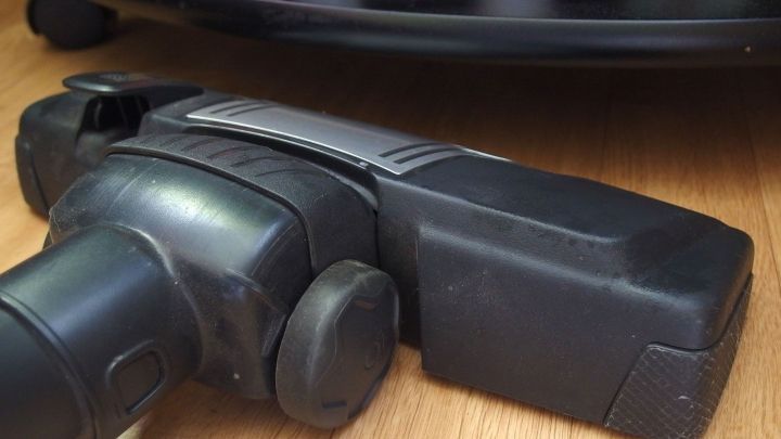 Ein Staubsaugerkopf liegt auf einem Holzboden und ist bereit, unter einem Regal zu saugen, um Staub zu entfernen.