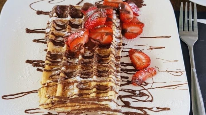 Eine Waffel mit Nutella liegt auf einem Teller, dekoriert mit frischen Erdbeeren und Schokoladensauce.