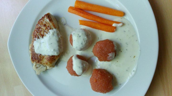 Auf einem Teller liegen saftige Tomaten-Kartoffel-Kl&ouml;&szlig;e neben gebratenem Fleisch und bunten Karottenstreifen.