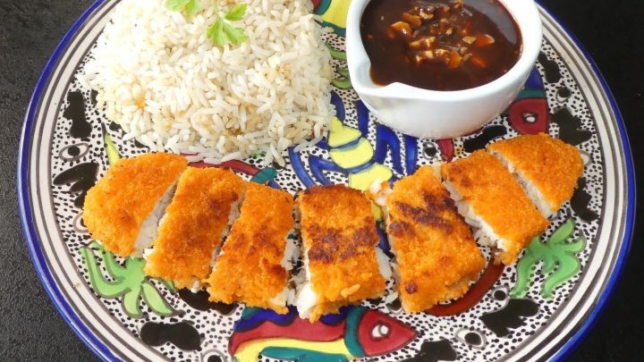 Kross gebratener Fisch liegt auf einem bunten Teller, umgeben von duftendem Reis und einer scharfen Knoblauchso&szlig;e.