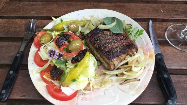 Ein sch&ouml;ner Teller mit gegrilltem Fleisch und buntem Salat steht auf einem Tisch aus Holz, umgeben von Kr&auml;utern und Weinflaschen.