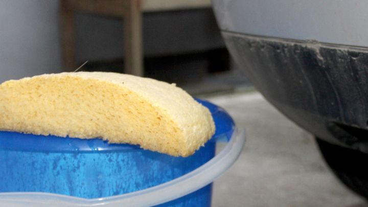 Ein Schwamm liegt auf einem blauen Eimer, w&auml;hrend das Auto gereinigt wird. Gratis-Autow&auml;sche im Winter wird vorbereitet.