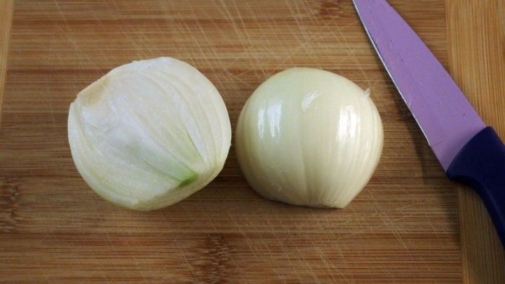 Zwei geschnittene Zwiebeln liegen auf einem Holzbrett neben einem K&uuml;chenmesser, bereit zur Zubereitung von Gerichten.