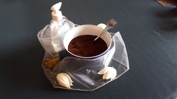 Eine Sch&uuml;ssel mit Kaffee-Peeling steht auf einem Tisch, umgeben von dekorativen Elementen und einem L&ouml;ffel.