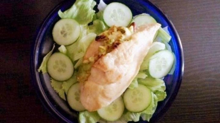 Eine gef&uuml;llte H&uuml;hnerbrust liegt auf einem Bett aus frischem Salat und Gurkenringen in einer blauen Sch&uuml;ssel.