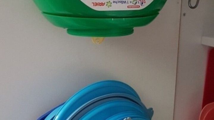 Ein gr&uuml;ner DIY-Halter f&uuml;r Kunststoffdeckel h&auml;ngt unter einem K&uuml;chenschrank und fasst mehrere farbige Deckel.