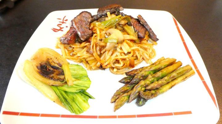 Saftiges Steak Teriyaki liegt auf einem wei&szlig;en Teller, umgeben von Pak Choi und gr&uuml;nem Spargel in einer asiatischen Anrichtung.