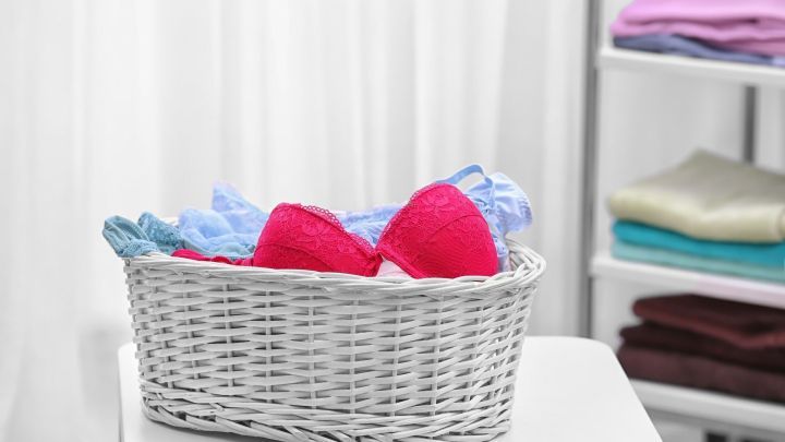 Rosa und blaue BHs liegen ordentlich in einem wei&szlig;en Korb auf einem Tisch, umgeben von einem hellen Raum mit W&auml;sche.