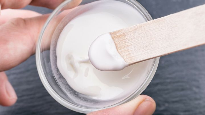 Eine Hand h&auml;lt einen Holzspatel, der eine dicke, wei&szlig;e Paste aus einem Glasbeh&auml;lter hebt, um Fettspritzer an der Wand zu entfernen.