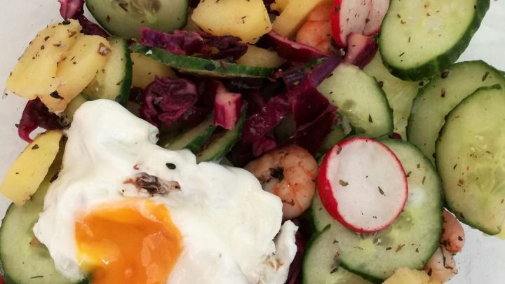 Bunter Kartoffelsalat mit Garnelen, Gurken, Rotkraut, Radieschen und einem Spiegelei in einer Sch&uuml;ssel, frisch angerichtet.