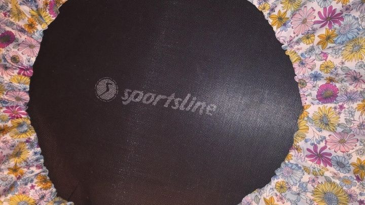 Eine runde Trampolin-Randabdeckung mit buntem Blumenmuster umrahmt das schwarze Sprungtuch in einem hellen Raum.