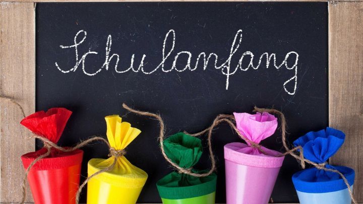 Bunte Schult&uuml;ten stehen nebeneinander vor einer Tafel, auf der &bdquo;Schulanfang&ldquo; in sch&ouml;ner Schrift geschrieben ist.