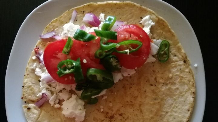 Ein Pfannkuchen wird gef&uuml;llt mit Schafsk&auml;se, Tomaten und Grillpaprika auf einem wei&szlig;en Teller pr&auml;sentiert.