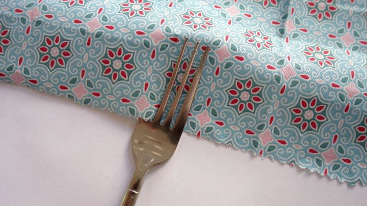 Ein bunter Stoff liegt ausgebreitet, w&auml;hrend eine Gabel darin platziert ist, um Bundfalten zu n&auml;hen.